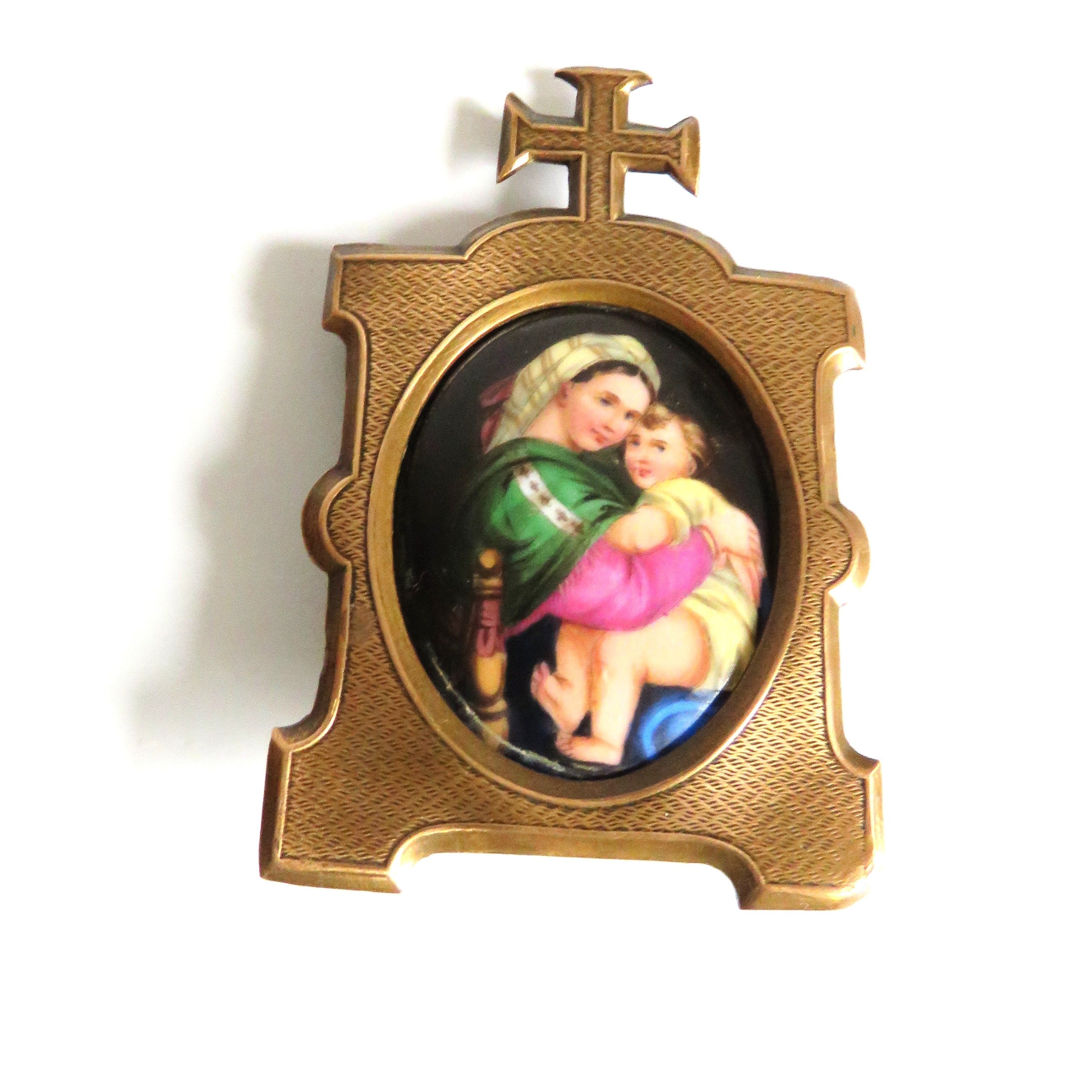 An antique  brass  frame featuring  an oval inset  Madonna della Saggiola by Raphael set against a plain white background.