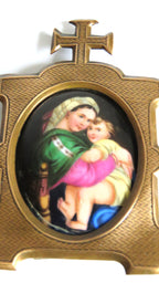 A close-up vintage brass  frame featuring  an oval inset  Madonna della Saggiola by Raphael set against a plain white background.