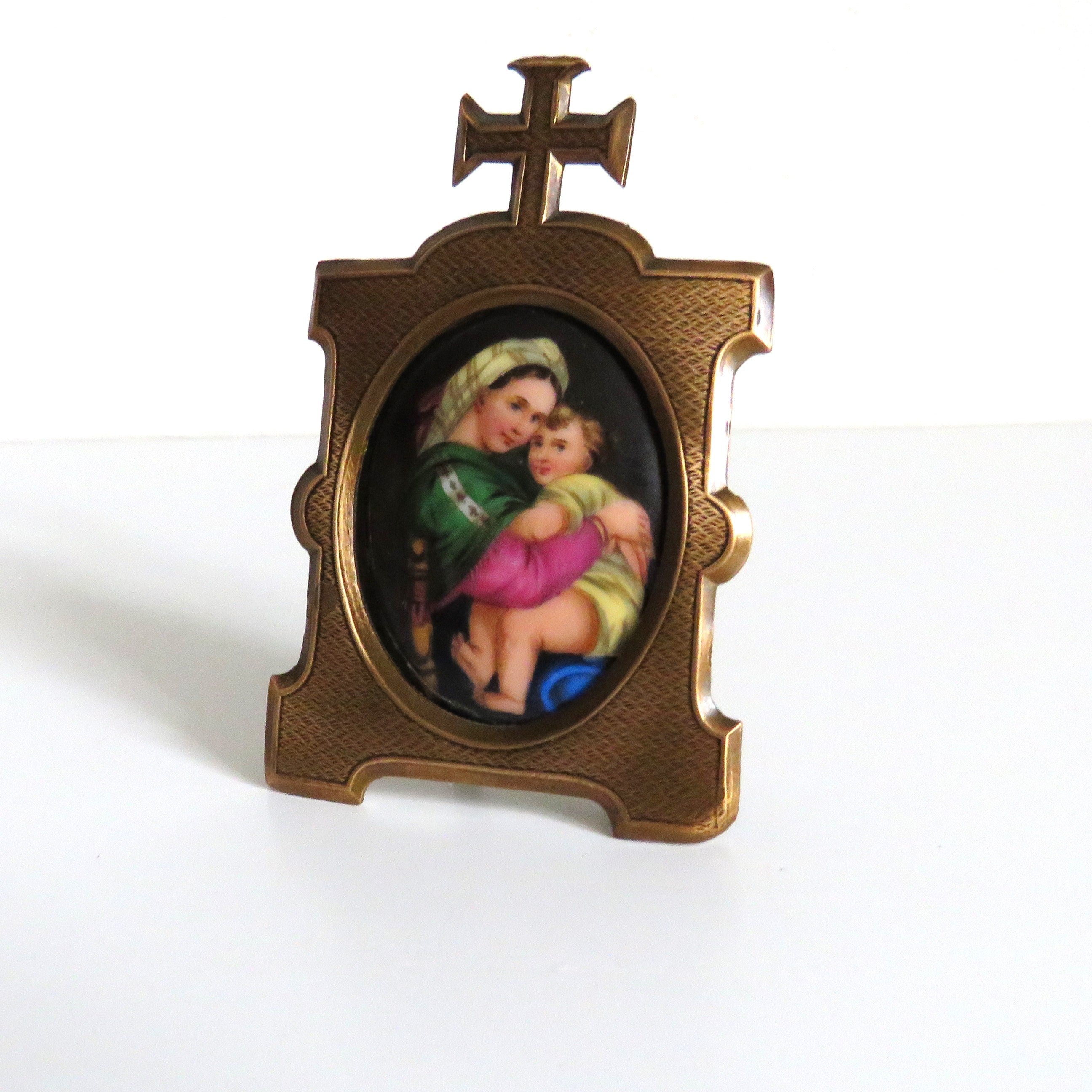 An antique  brass  frame featuring  an oval inset  Madonna della Saggiola by Raphael set against a plain white background.