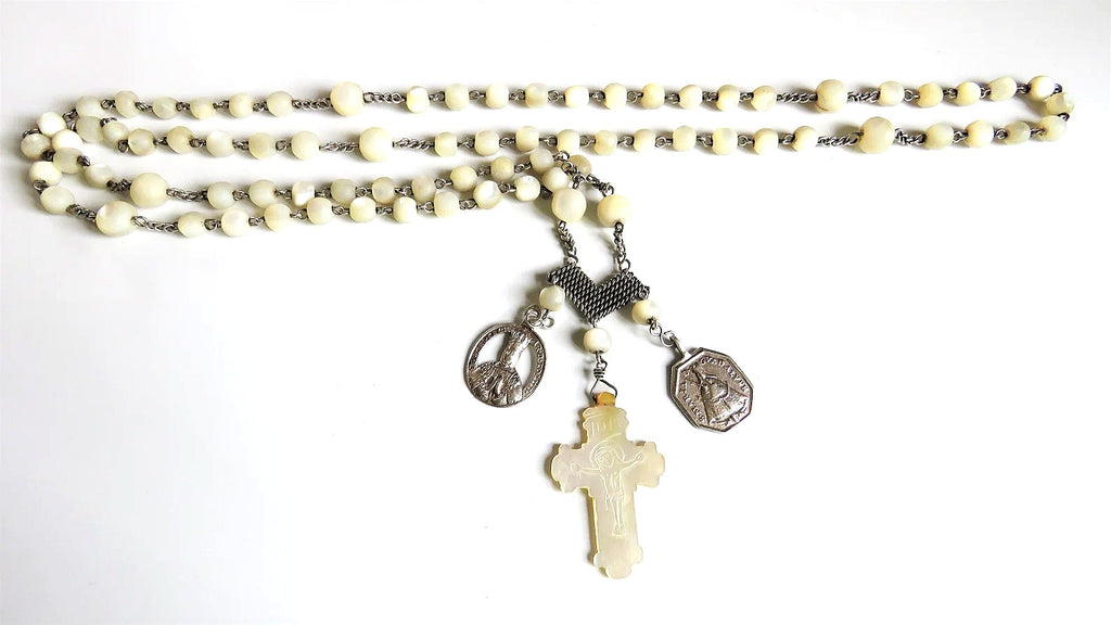 Close-up of an antique French silver rosary with a carved mother-of-pearl crucifix and articulated silver heart centre, showing luminous creamy beads and intricate silver devotional chainwork.