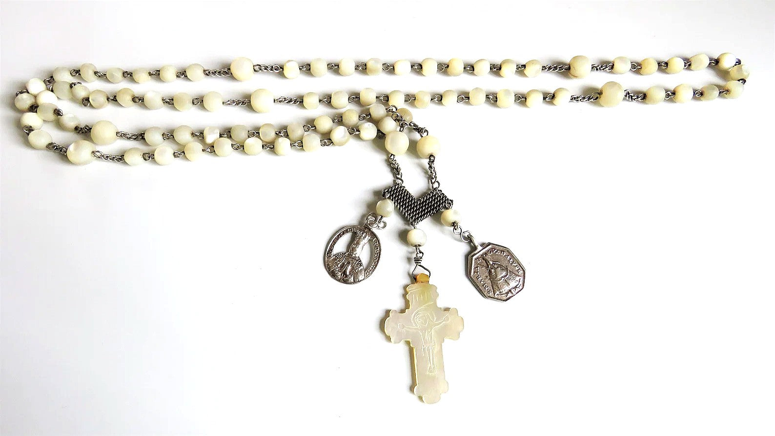 Close-up of an antique French silver rosary with a carved mother-of-pearl crucifix and articulated silver heart centre, showing luminous creamy beads and intricate silver devotional chainwork.