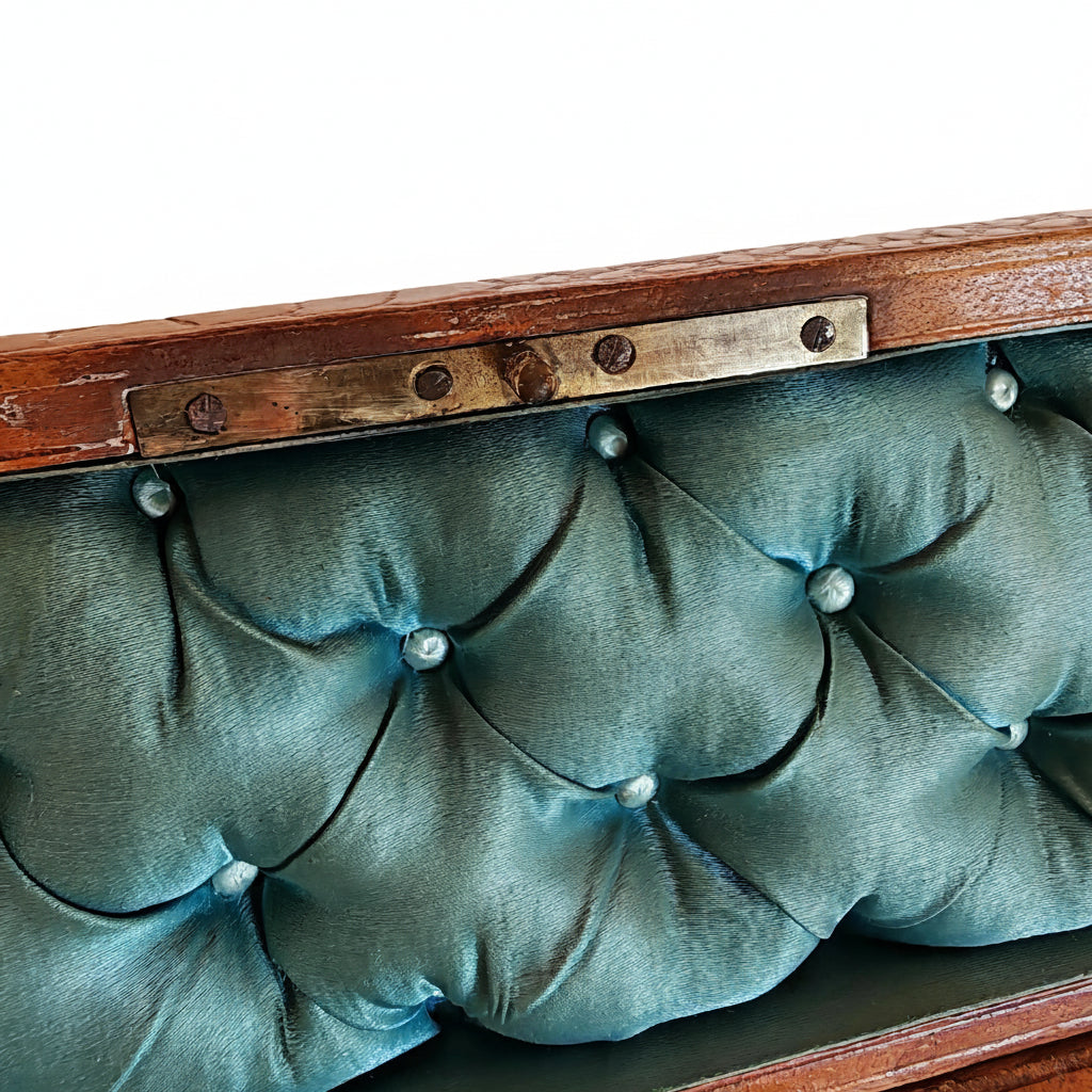 Close-up of a vintage leather chest  with a teal green tufted silk 
front and a brass latch.
