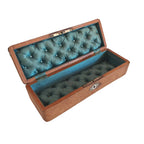 An open vintage wooden jewelry box with a tufted teal-green silk interior, resting on a white wooden surface.