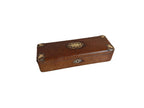 A rectangular vintage wooden box with a textured brown leather or faux-leather finish, featuring decorative oval and circular metal corner accents and a central oval medallion on the lid, resting on a light-colored wooden surface.