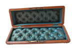 An open wooden coffin-shaped box with tufted teal upholstery inside, photographed against a plain off-white wall.